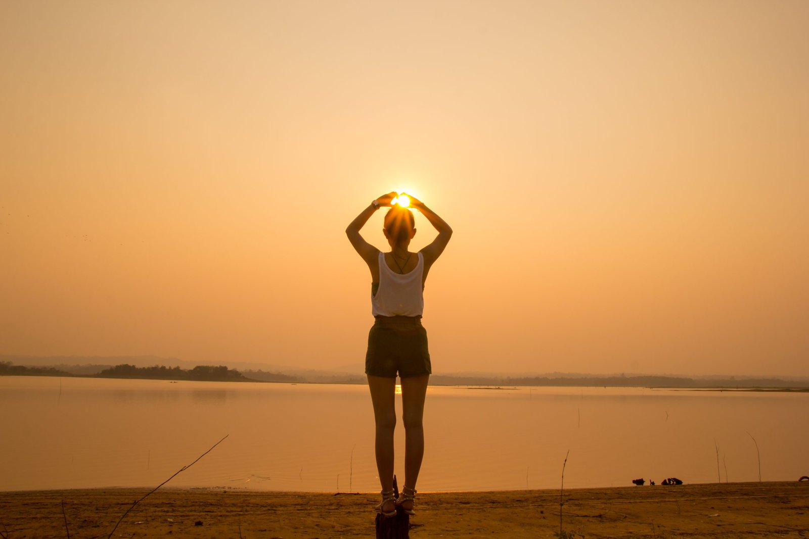 vista-trasera-de-una-mujer-haciendo-gestos-mientras-esta-de-pie-en-el-lago-contra-el-cielo-durante-la-puesta-de-sol