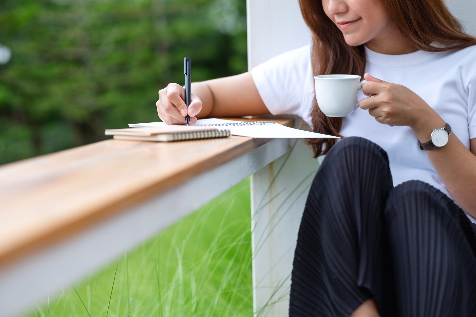 Closeup image of a beautiful young asian woman writing on a notebook in the outdoors